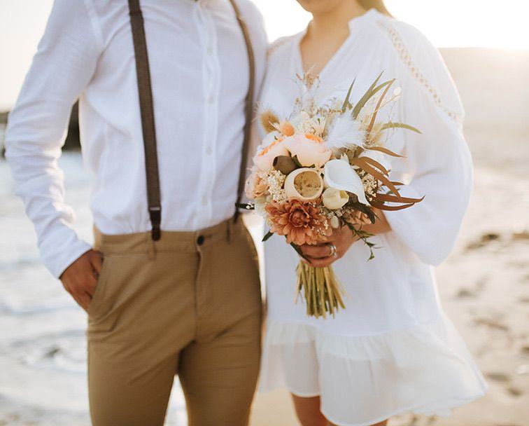 A couple on the sand holding a bouquet